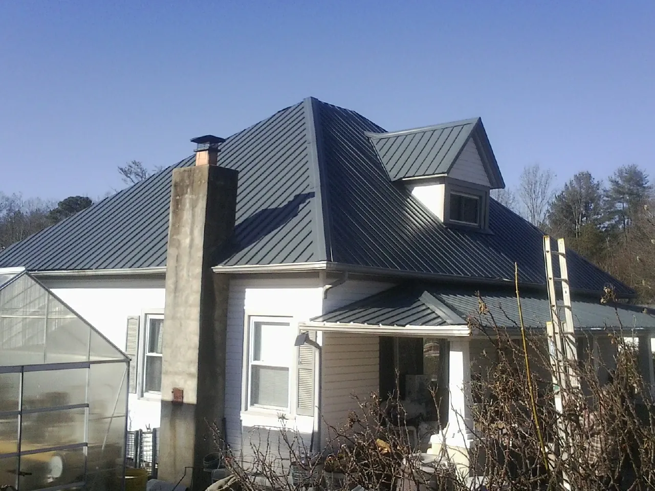 Dark blue standing seam metal roof on a white farmhouse with dormer — Slate & Tile Roof Repair by Roofing Brothers in Mackinaw