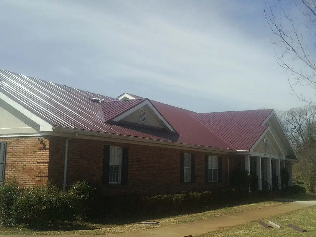 Red metal roof with gabled entries on a long brick building, from a Hail Damage Roof Repair job in Mackinaw