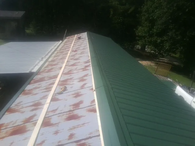 Old rusted panels beside newly installed green metal roofing — Wind Damage Roof Repair by Roofing Brothers in Mackinaw