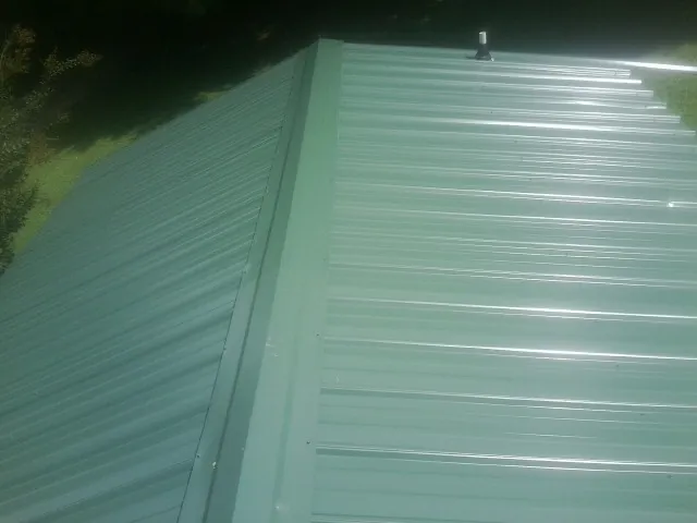 New green metal panels meeting at the ridge of a roof — Flat Roof Repair work by our crew in Mackinaw