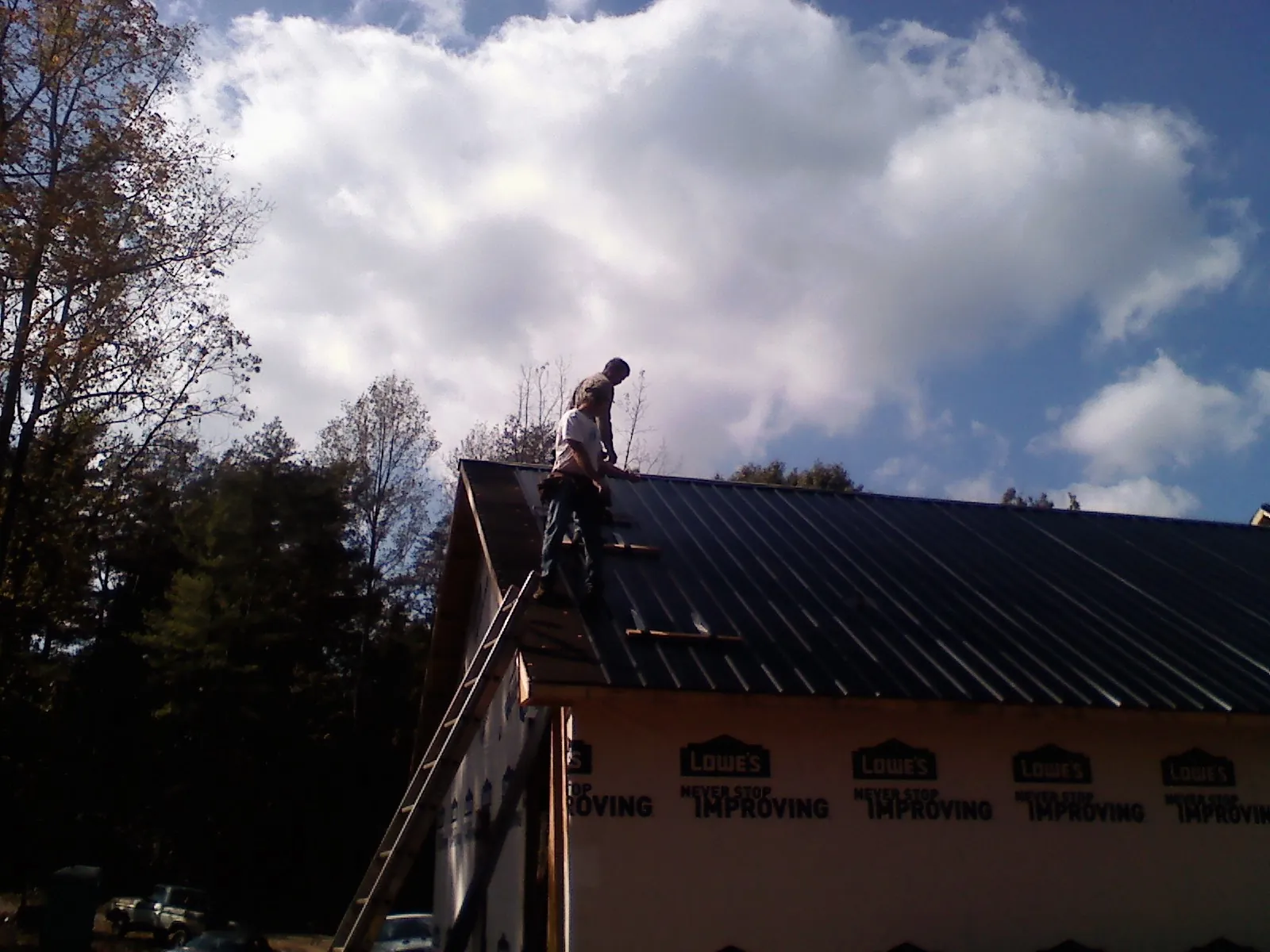 Roofer fastening dark metal panels high against a cloudy sky, from a Roof Inspection job in Mackinaw