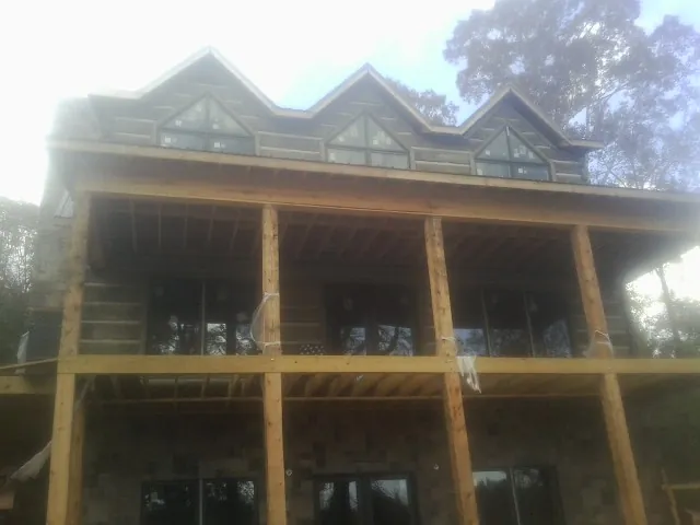 Dormers and porch framing on a large log home under construction — Roof Coating work by our crew in Mackinaw