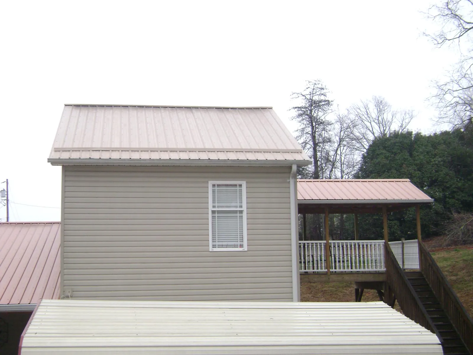 Tan metal roofs on a two story addition and attached porch, from a Roof Replacement job in Mackinaw