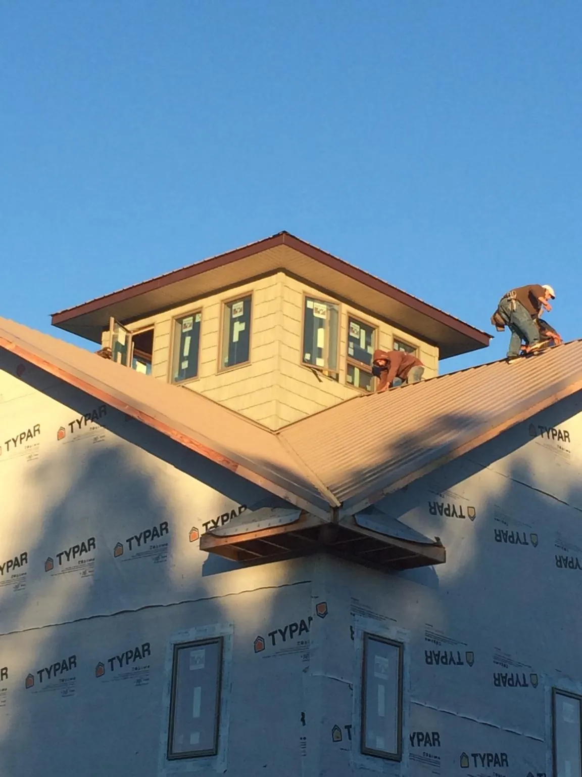 Roofers working around a rooftop cupola on a new metal roof at sunset — Roof Waterproofing in Mackinaw by Roofing Brothers